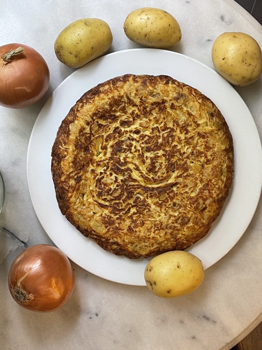 Tortilla de Patata y cebolla en un plato con ingredientes base a su alrededor, a la venta en el Obrador de la nena, Barcelona